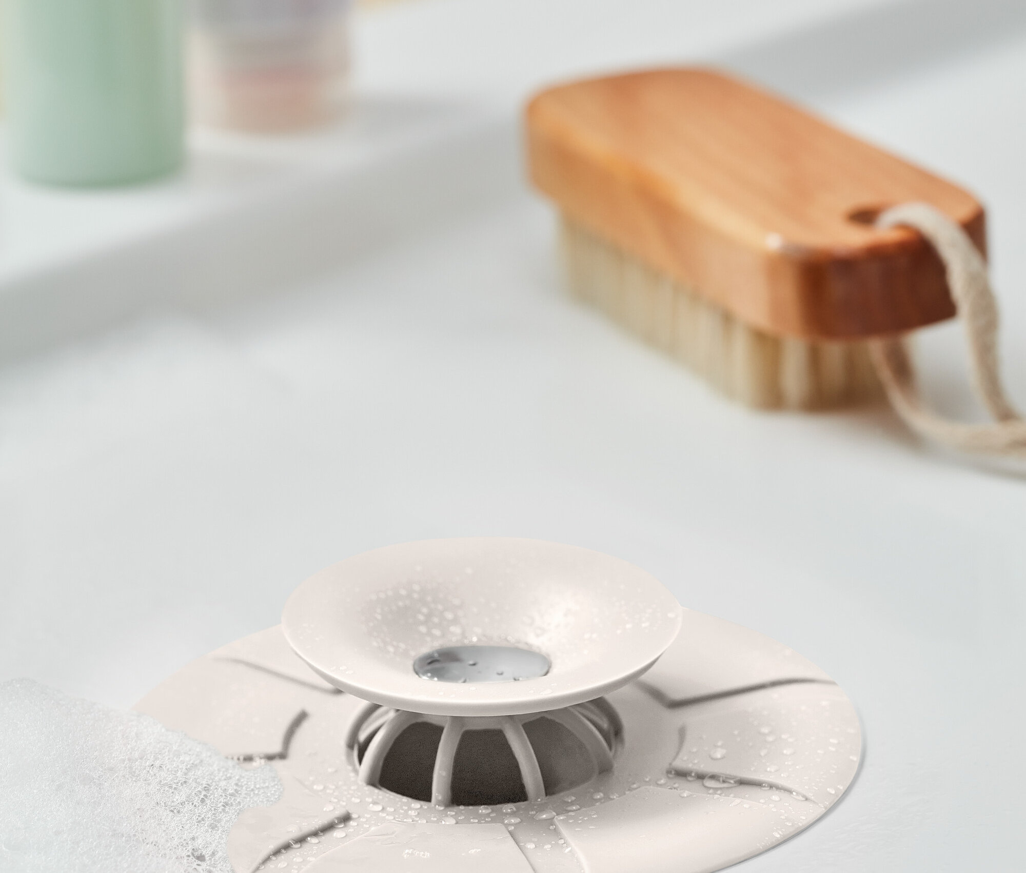 Gros plan d'un lavabo avec un piège anti-saleté blanc au centre. À l'arrière-plan, une brosse et des bouteilles.