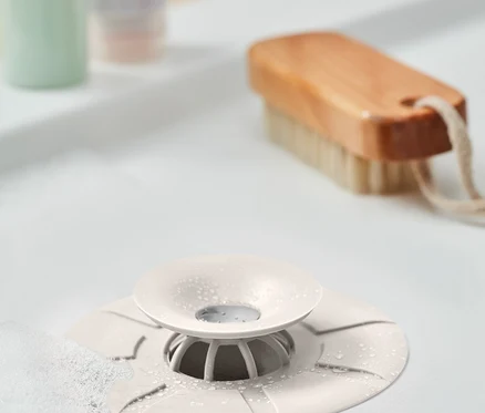 Gros plan d'un lavabo avec un piège anti-saleté blanc au centre. À l'arrière-plan, une brosse et des bouteilles.