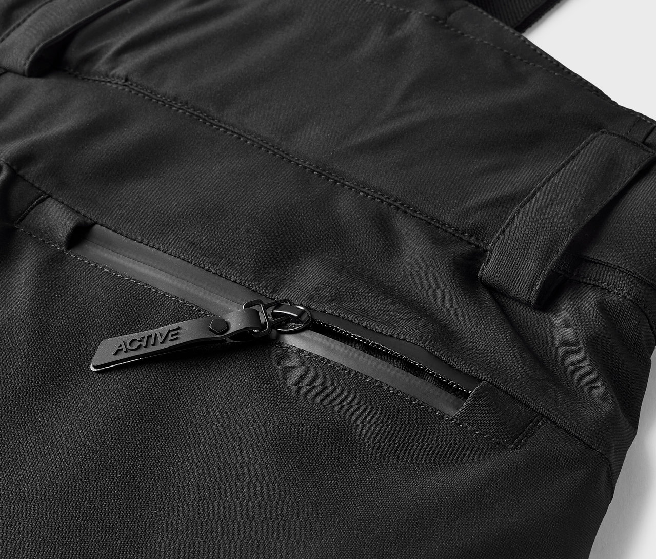 Détail d'un pantalon noir avec une poche zippée et un curseur portant l'inscription ACTIVE.