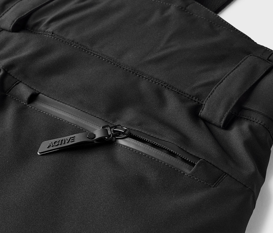 Détail d'un pantalon noir avec une poche zippée et un curseur portant l'inscription ACTIVE.