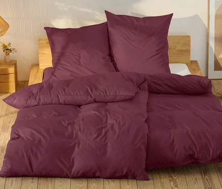 Linge de lit bordeaux sur un lit avec un cadre en bois.