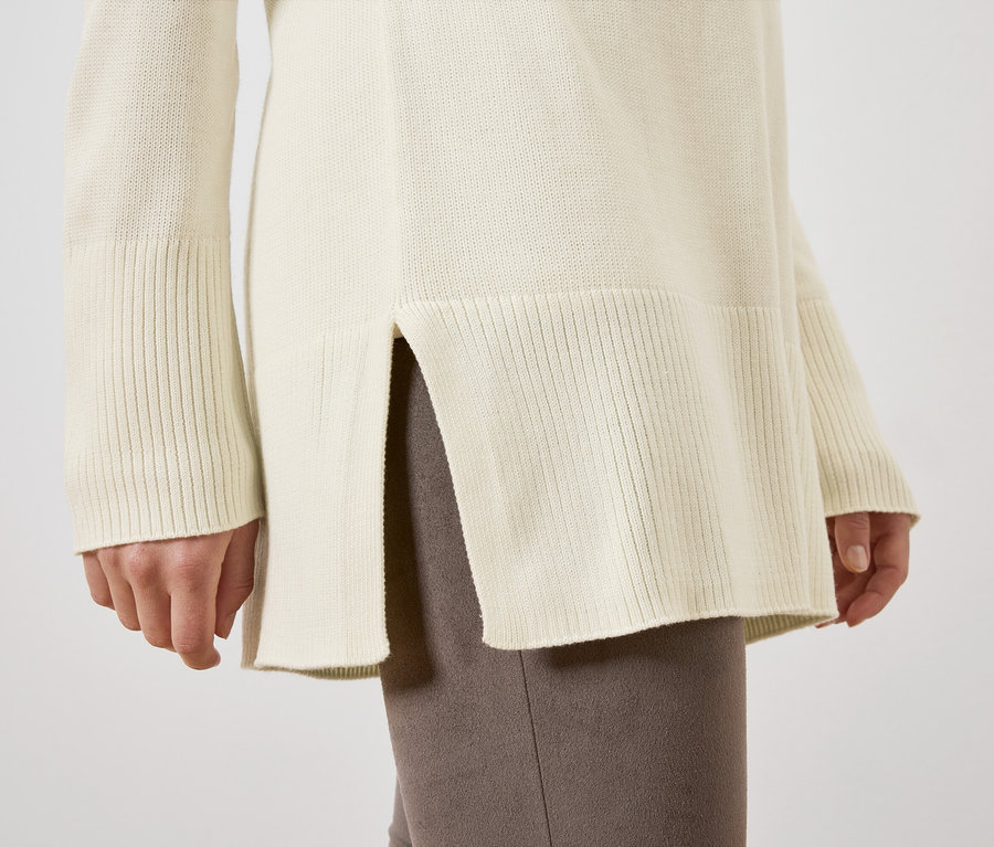 Gros plan sur un long pull en maille crème porté par une femme.