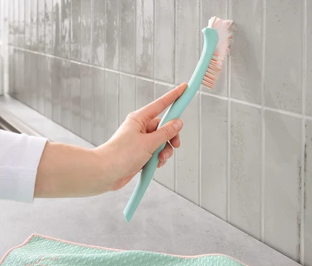 Une main nettoie les joints sales sur les carreaux avec une brosse à joints.