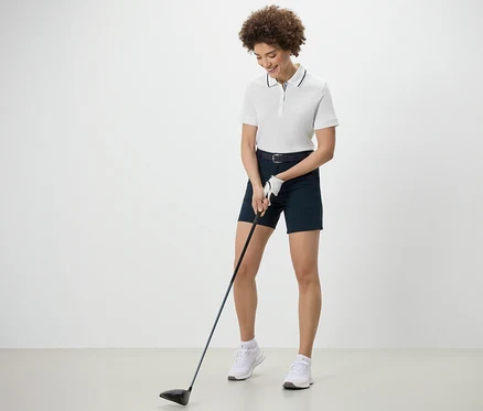 Femme jouant au golf et portant un polo technique blanc.