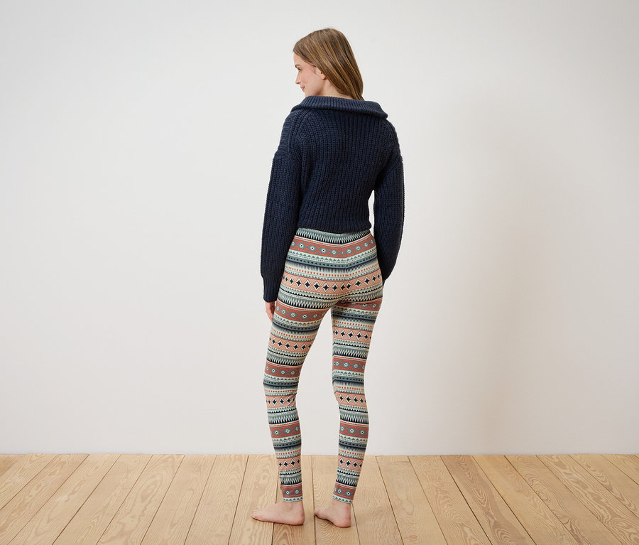 Une femme portant un pull bleu marine et des leggings à motifs, dos à la caméra.