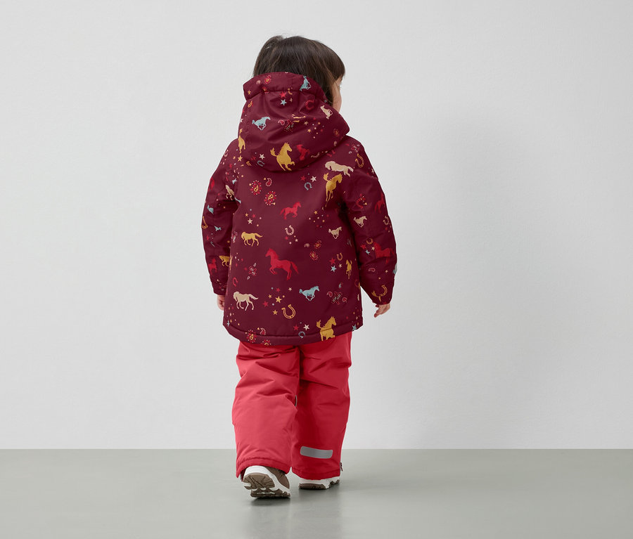 Garçon portant une veste d'hiver avec un imprimé de cheval et un pantalon rouge, dos à la caméra.