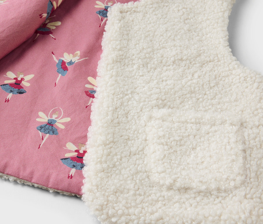 Détail d'un gilet pour enfant avec une doublure rose imprimée de ballerines et un extérieur en sherpa blanc.