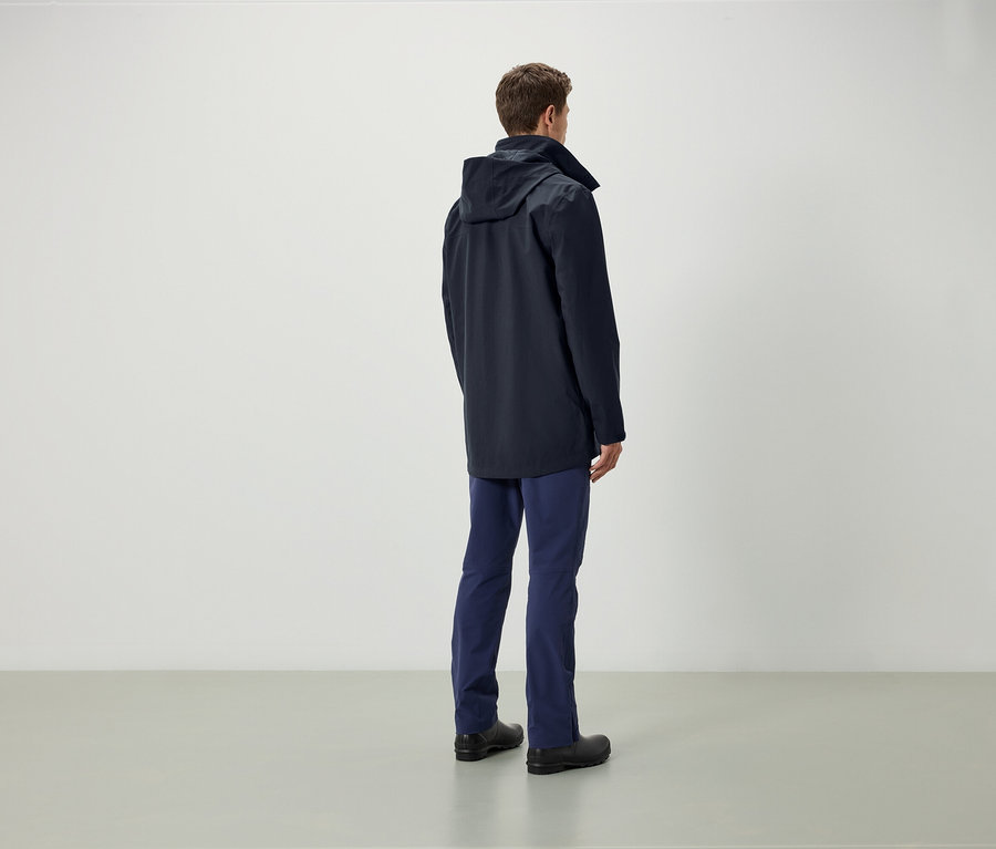 Homme de dos, portant une veste bleue à capuche, un pantalon bleu et des chaussures noires.