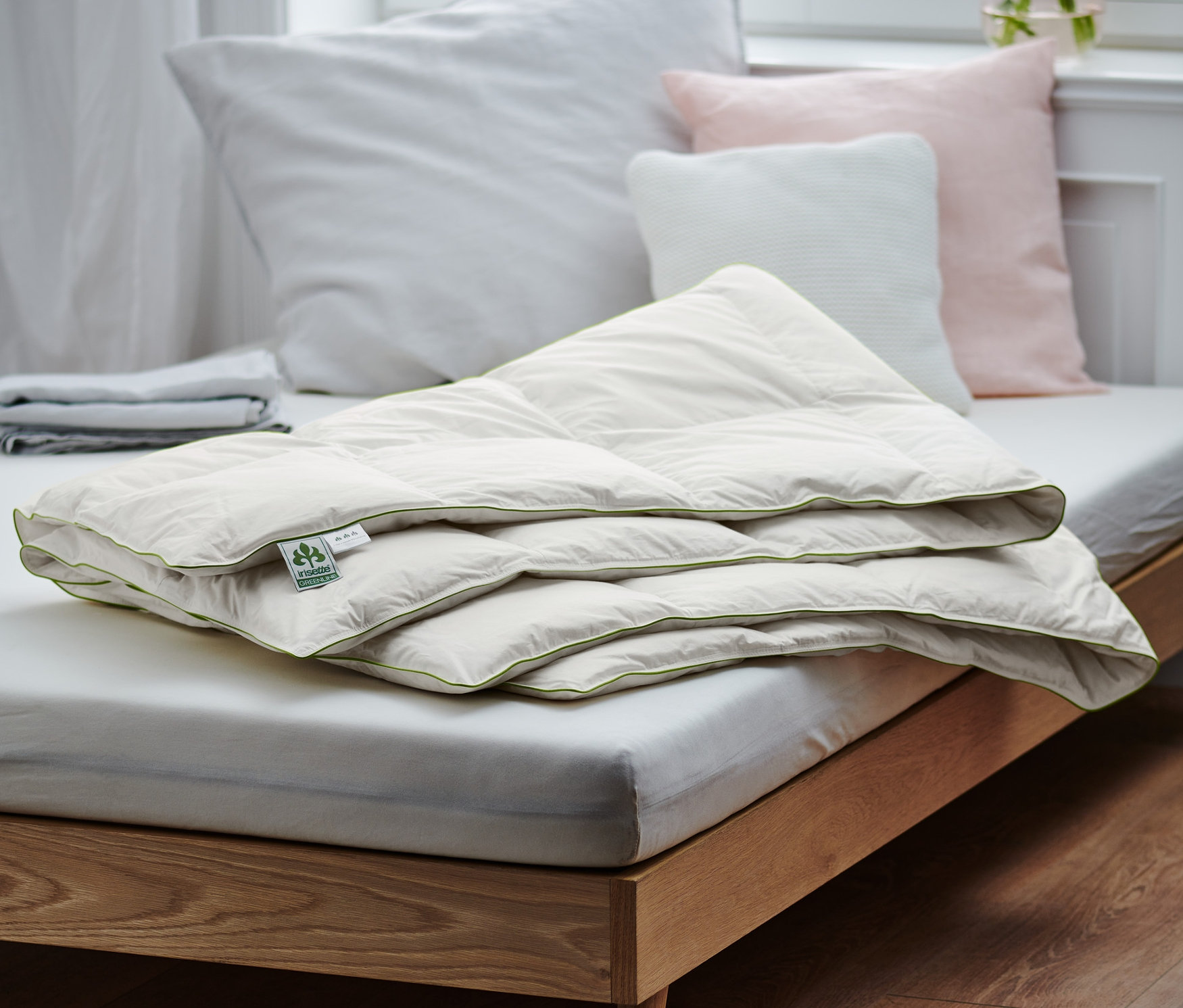 Une couette mi-saison en duvet irisette® pliée est posée sur un lit.