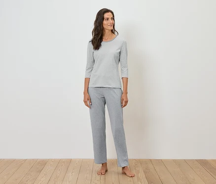 Une femme debout porte un pyjama gris.