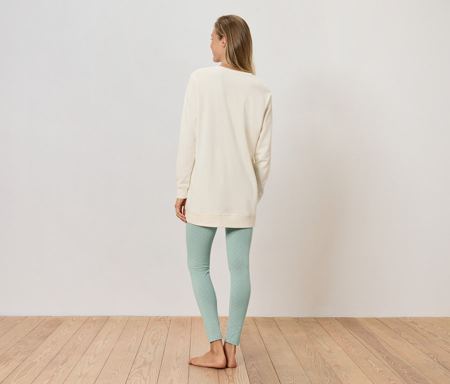 Une femme se tient dos à l'appareil photo, portant un sweat-shirt couleur crème et un legging vert clair.