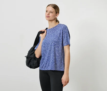 Une femme portant un t-shirt bleu à motifs et des leggings noirs, avec un sac à dos noir sur l'épaule.