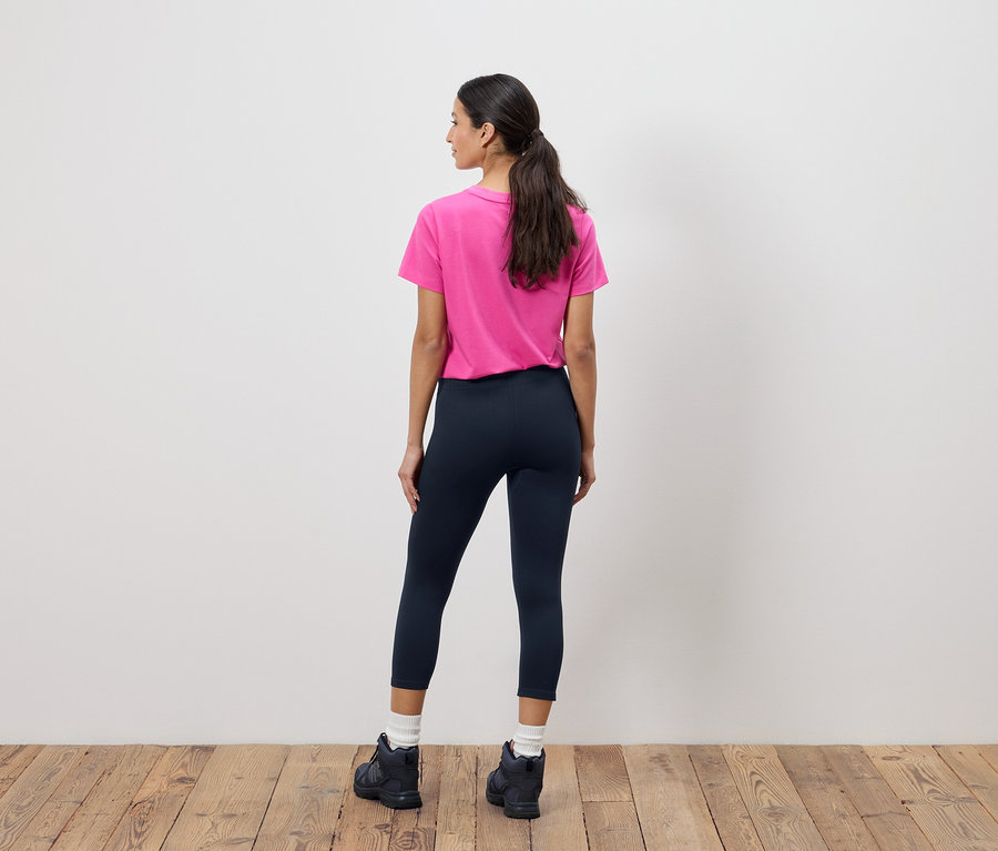 Vue arrière d'une femme avec une queue de cheval portant un t-shirt rose, un legging bleu marine et des bottes noires.