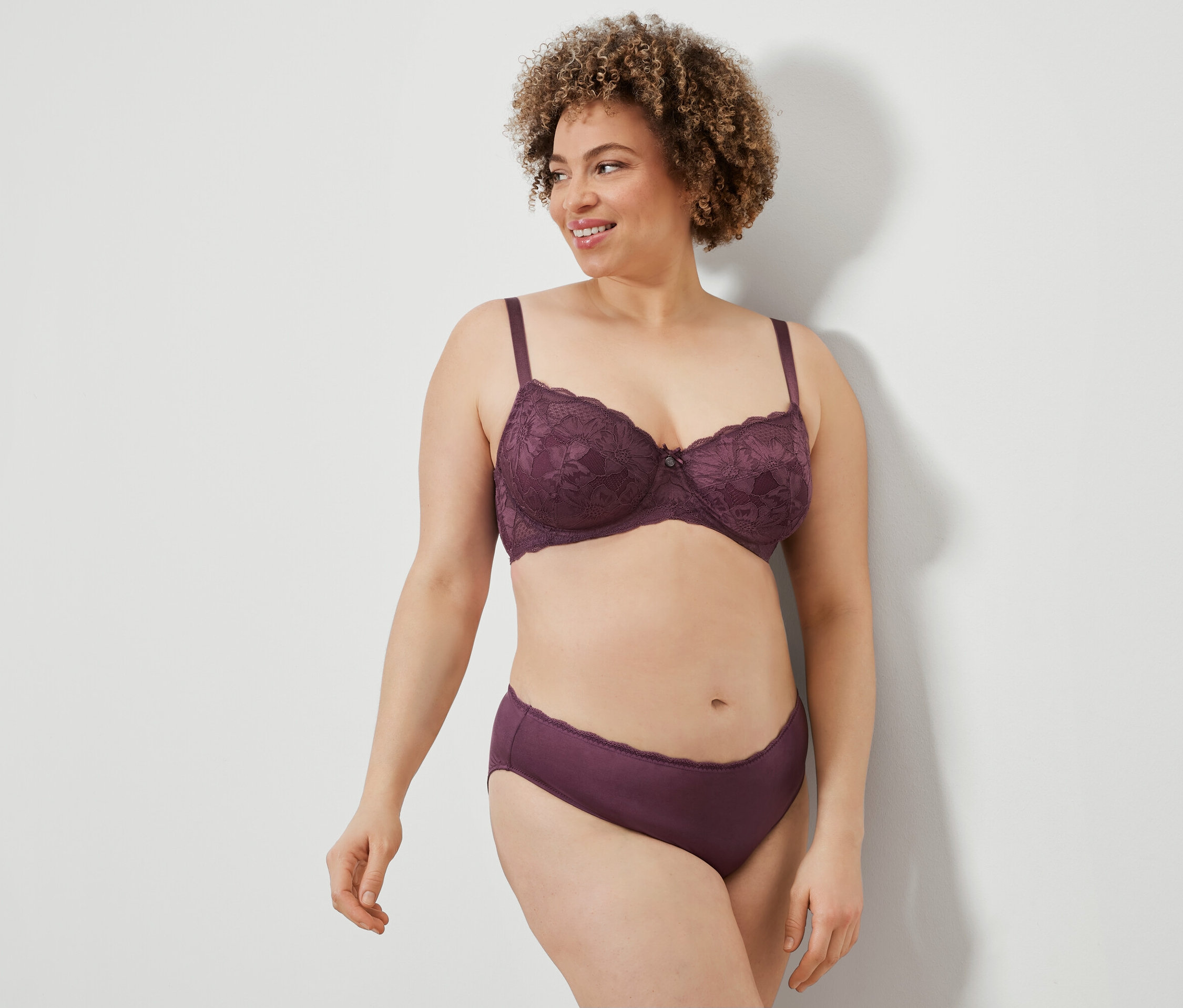 Femme aux cheveux bouclés posant en soutien-gorge et culotte en dentelle violette.