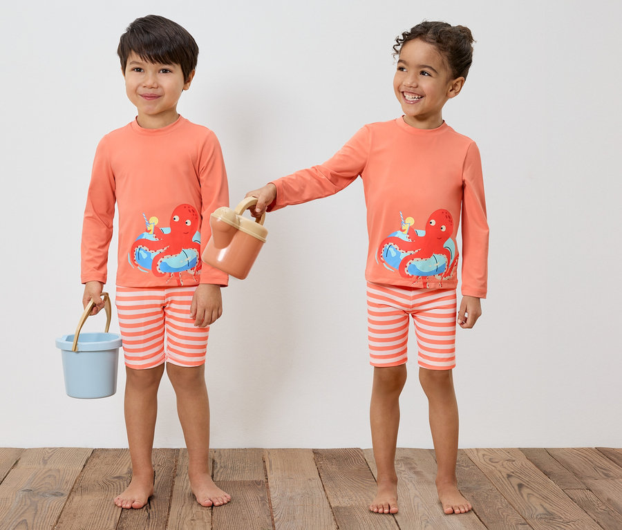 Deux enfants portant des hauts à manches longues orange assortis avec un motif de poulpe et des slips de bain rayés tiennent des seaux de jouets.