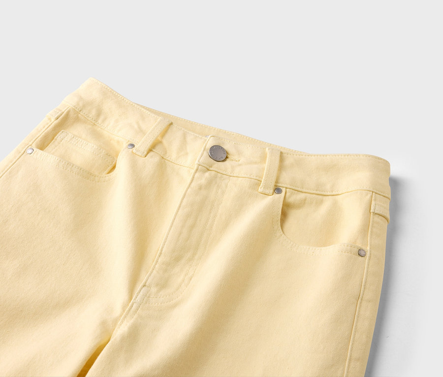 Gros plan d'un jean jaune clair avec des poches, des passants de ceinture et un bouton argenté.