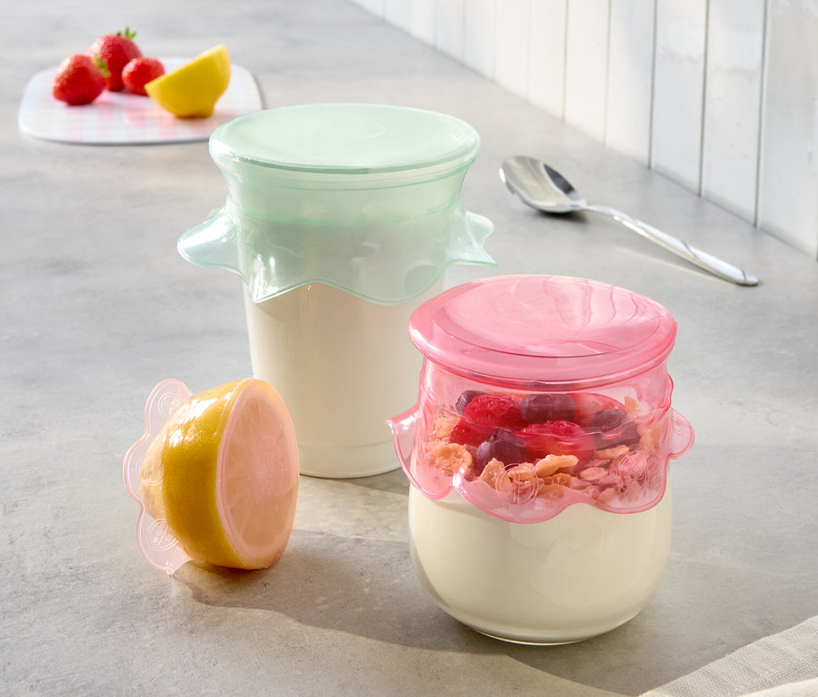 Sur un comptoir de cuisine, deux pots de yaourt avec des couvercles roses et menthe et un demi-citron avec un couvercle rose.
