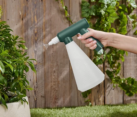 Une main vaporise une plante d'intérieur avec un vaporisateur vert et blanc devant une clôture en bois.