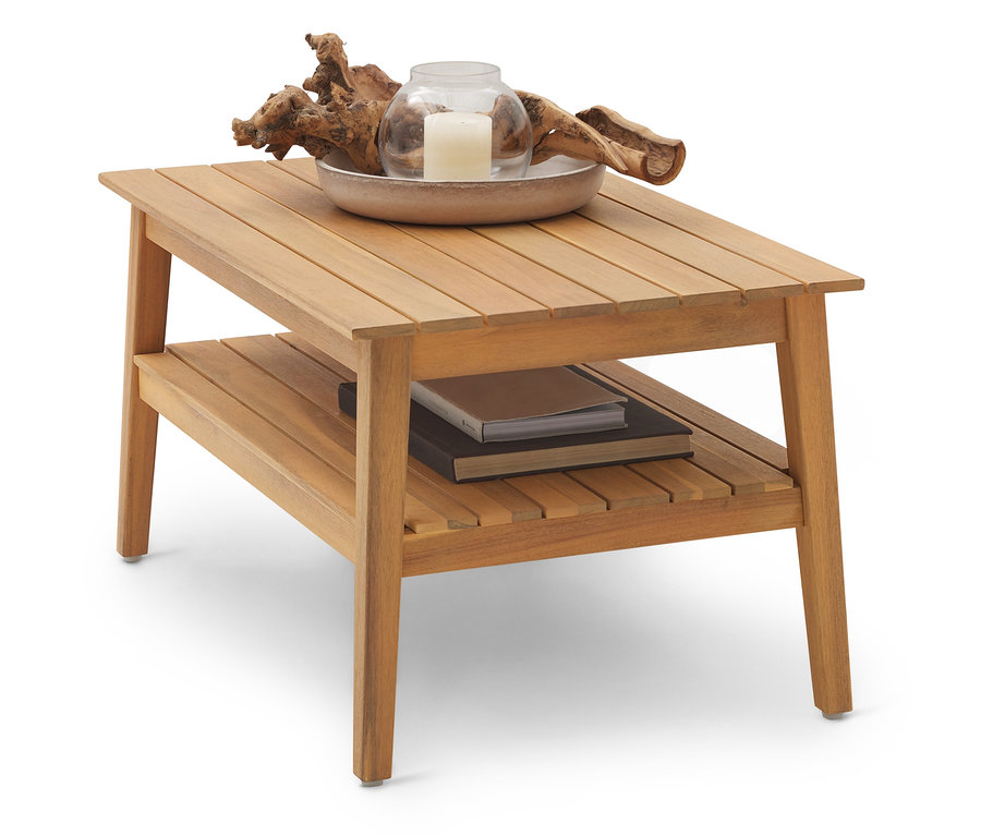 Une table basse en bois marron clair avec deux niveaux. Sur le niveau supérieur se trouvent un bol avec une bougie et du bois flotté, et sur le niveau inférieur se trouvent des livres.