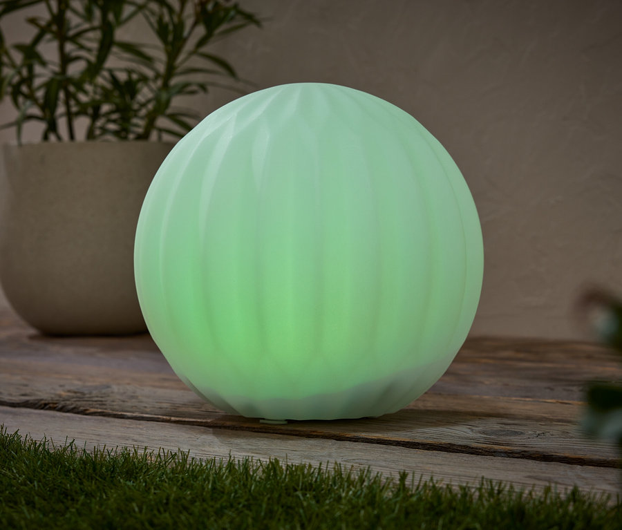 Une lampe sphérique verte repose sur une surface en bois, à côté d'une plante en pot.