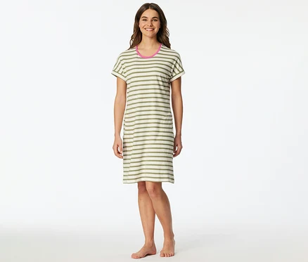 Une femme souriante est debout pieds nus, vêtue d'une chemise de nuit SCHIESSER à rayures horizontales vert olive et blanc cassé avec un liseré rose au col.