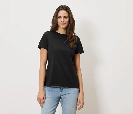 Une femme aux cheveux ondulés porte un t-shirt noir et un jean.