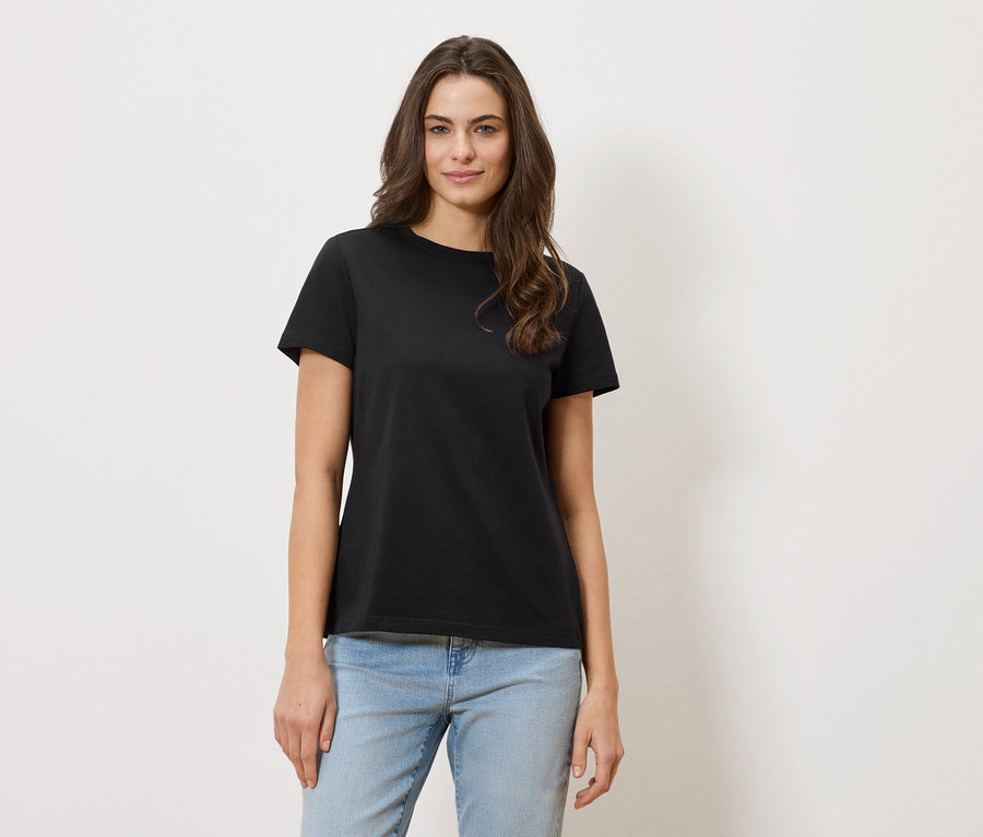 Une femme aux cheveux ondulés porte un t-shirt noir et un jean.