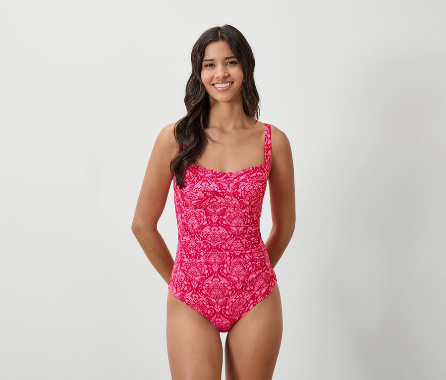 Femme aux cheveux foncés portant un maillot de bain rose à motif floral et col carré, souriant.