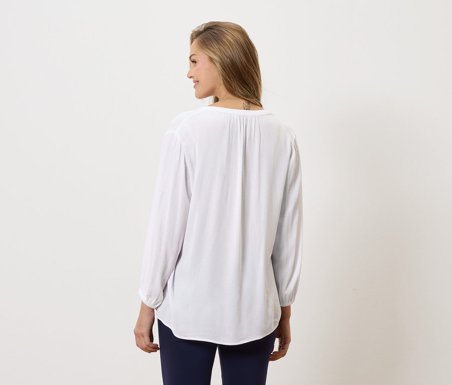 Femme vue de dos, portant une longue blouse blanche et un pantalon bleu.