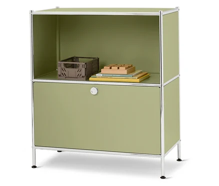 Une armoire verte avec un cadre argenté se dresse sur un fond blanc. Une caisse marron, des livres et un jouet en bois sont posés sur l'étagère supérieure.