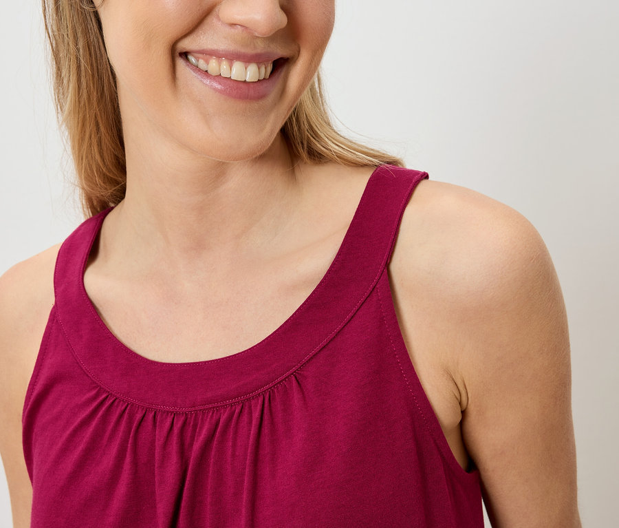 Gros plan d'une femme souriante portant un haut sans manches bordeaux.