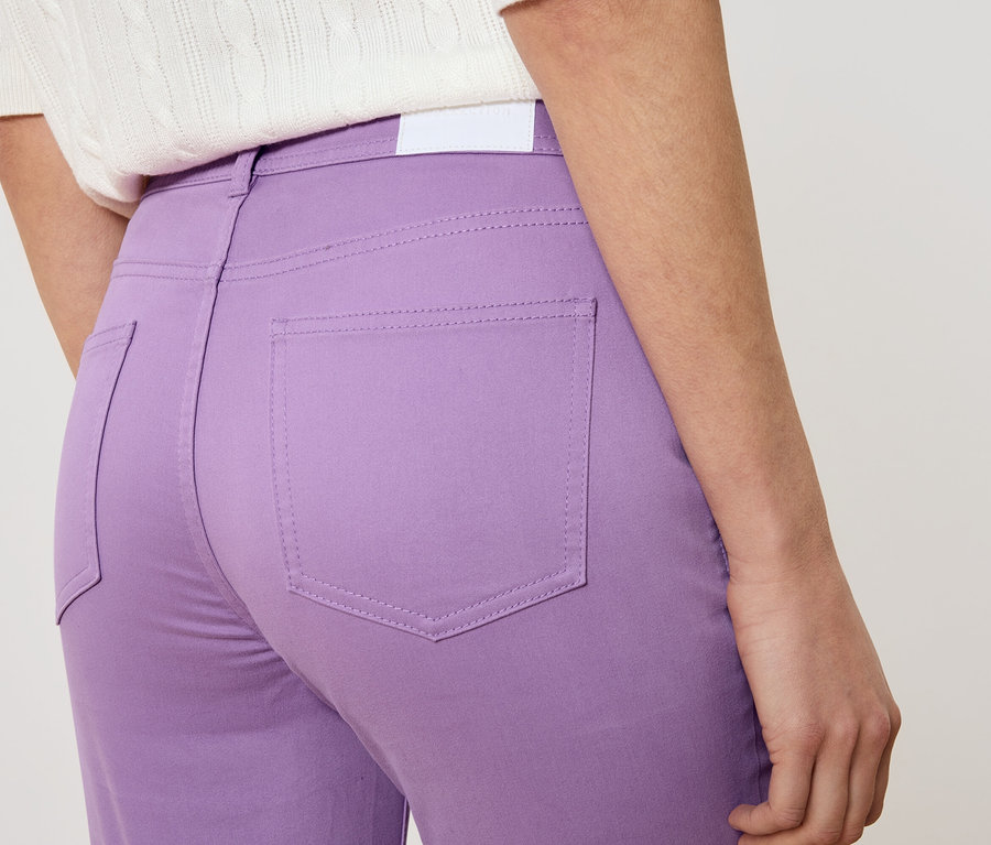 Gros plan d'une femme vue de dos portant un pantalon violet et un haut blanc.