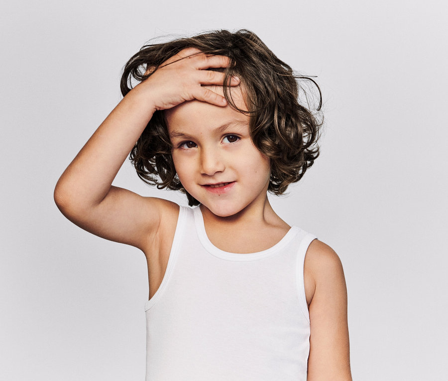 Portrait d'un enfant aux cheveux bruns bouclés et portant un maillot de corps blanc, posant une main sur son front.