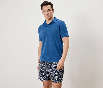 Homme portant un polo bleu et un short de bain à motifs.