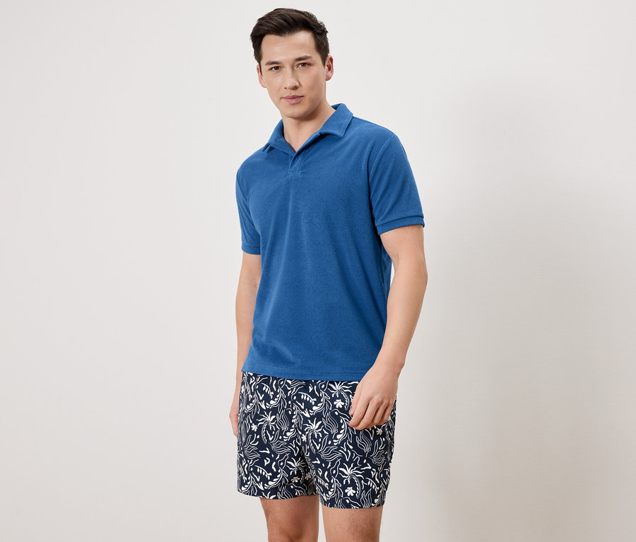 Homme portant un polo bleu et un short de bain à motifs.
