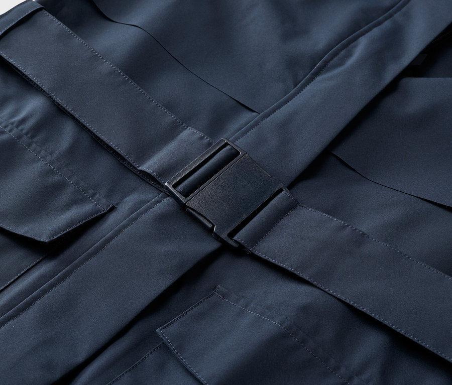 Gros plan sur une veste bleu marine avec des poches et une fermeture à boucle noire.