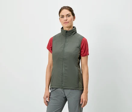 Une femme debout porte un gilet vert olive sur un t-shirt rouge, associé à un pantalon gris.