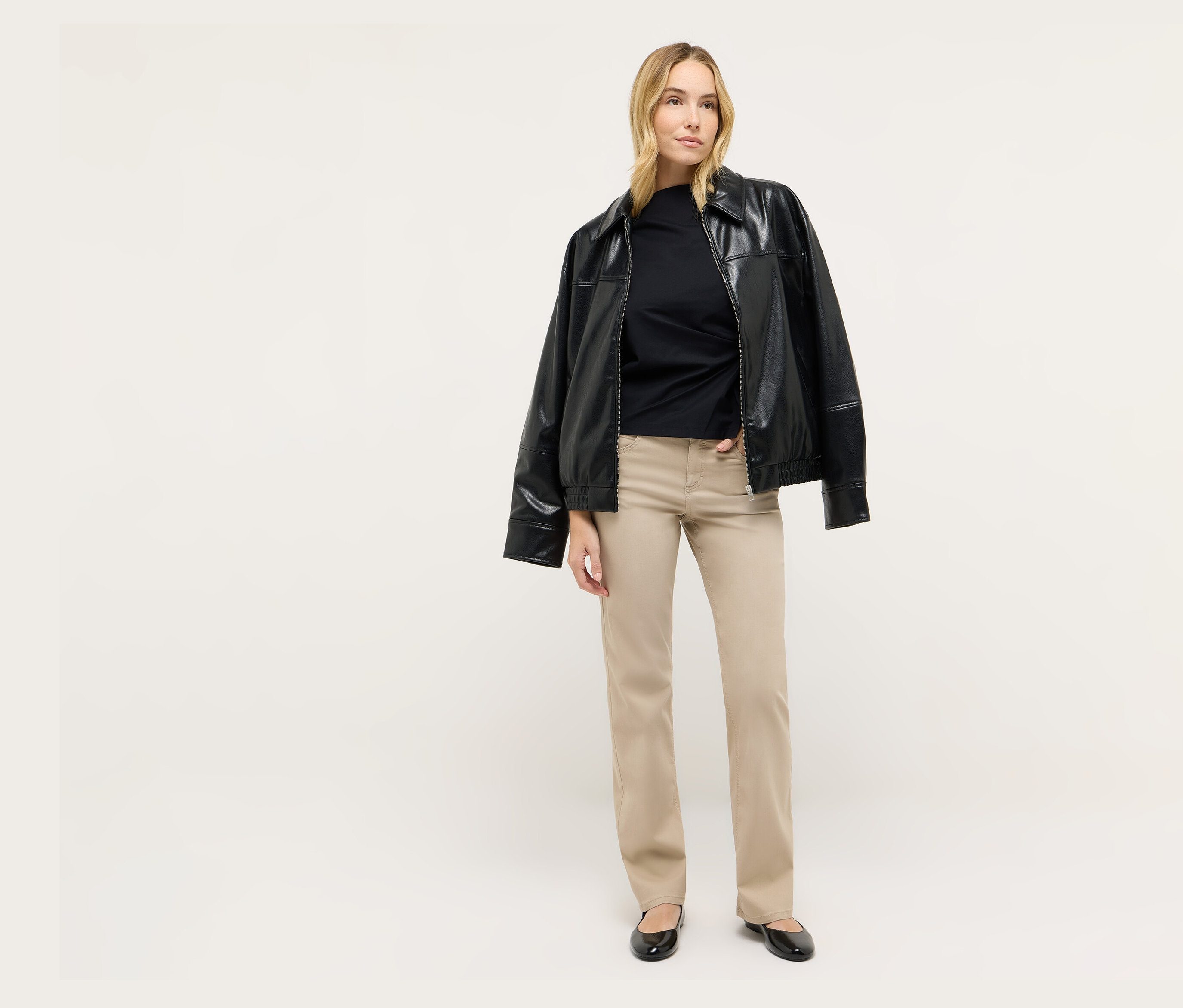 Une femme blonde se tient debout et porte une veste noire et un jean Angels Denim «
Ara
A», Straight Fit.