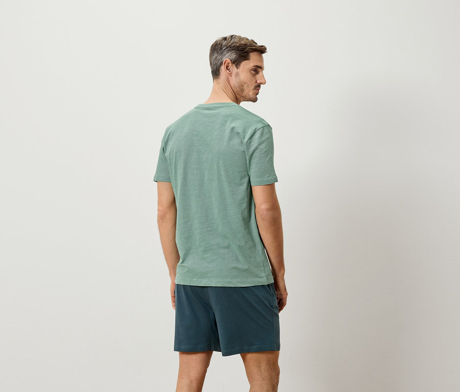 Homme vu de dos, portant un t-shirt vert et un short bleu.