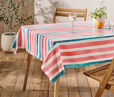 Table à manger recouverte d'une nappe rayée rouge, blanche et turquoise, décorée de vaisselle, de verres, d'une carafe, d'une plante et d'une orange.