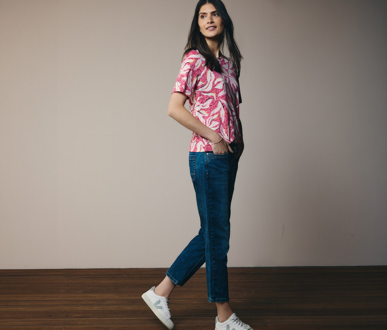Une femme marche avec un t-shirt manches courtes CECIL rose et un jean. Ses mains sont dans ses poches.