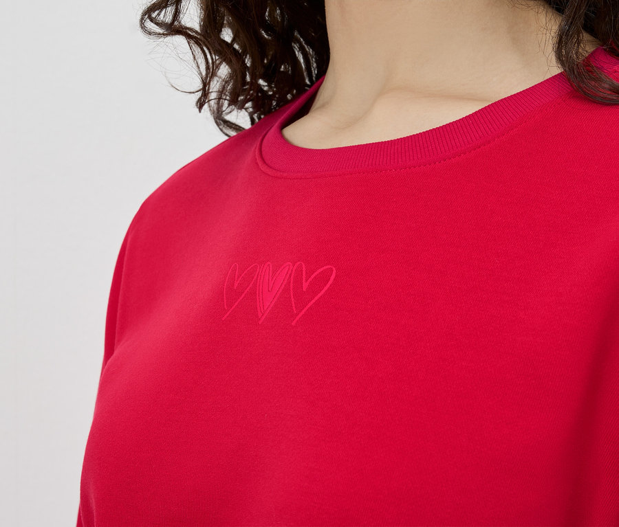 Gros plan d'une femme portant un sweat-shirt rouge avec trois petits cœurs.