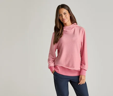 Une femme aux cheveux bruns porte un pull rayé rose et blanc et un pantalon bleu.