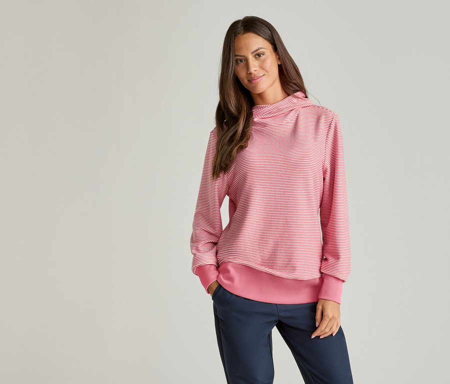 Une femme aux cheveux bruns porte un pull rayé rose et blanc et un pantalon bleu.