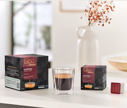 Packs de Qbo Espresso APANECA ANA de 27 et 8 capsules à côté d'un verre d'espresso et d'un seul cube de capsule.