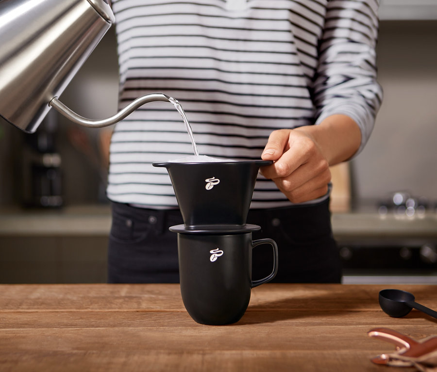 Une personne verse de l'eau d'une bouilloire dans un filtre à café manuel noir Gr. 101 avec un motif de grain, qui est placé sur une tasse.