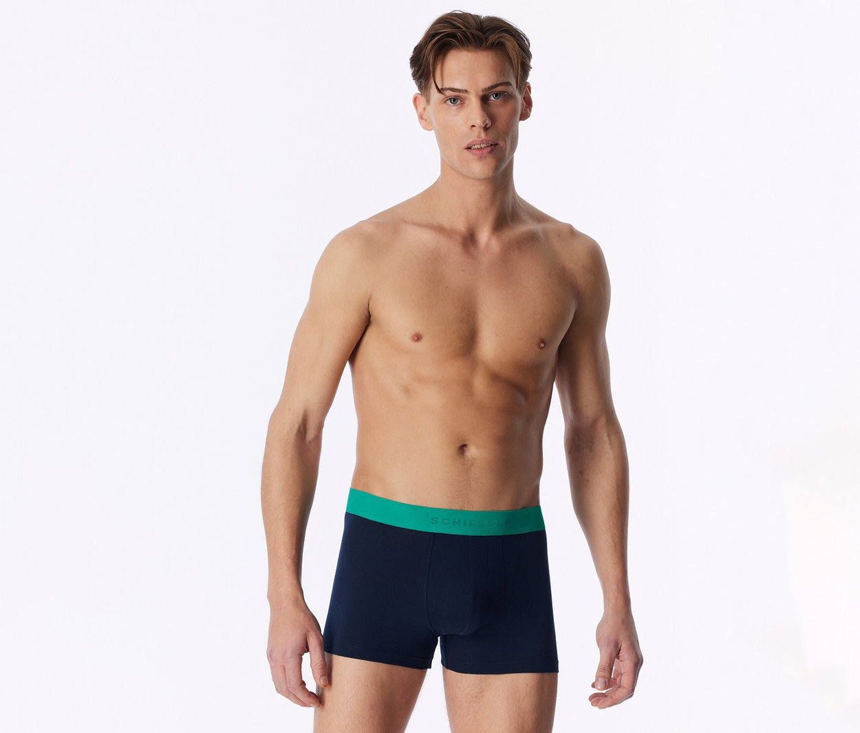 Un homme torse nu se tient de face, portant un boxer bleu marine avec une ceinture verte.