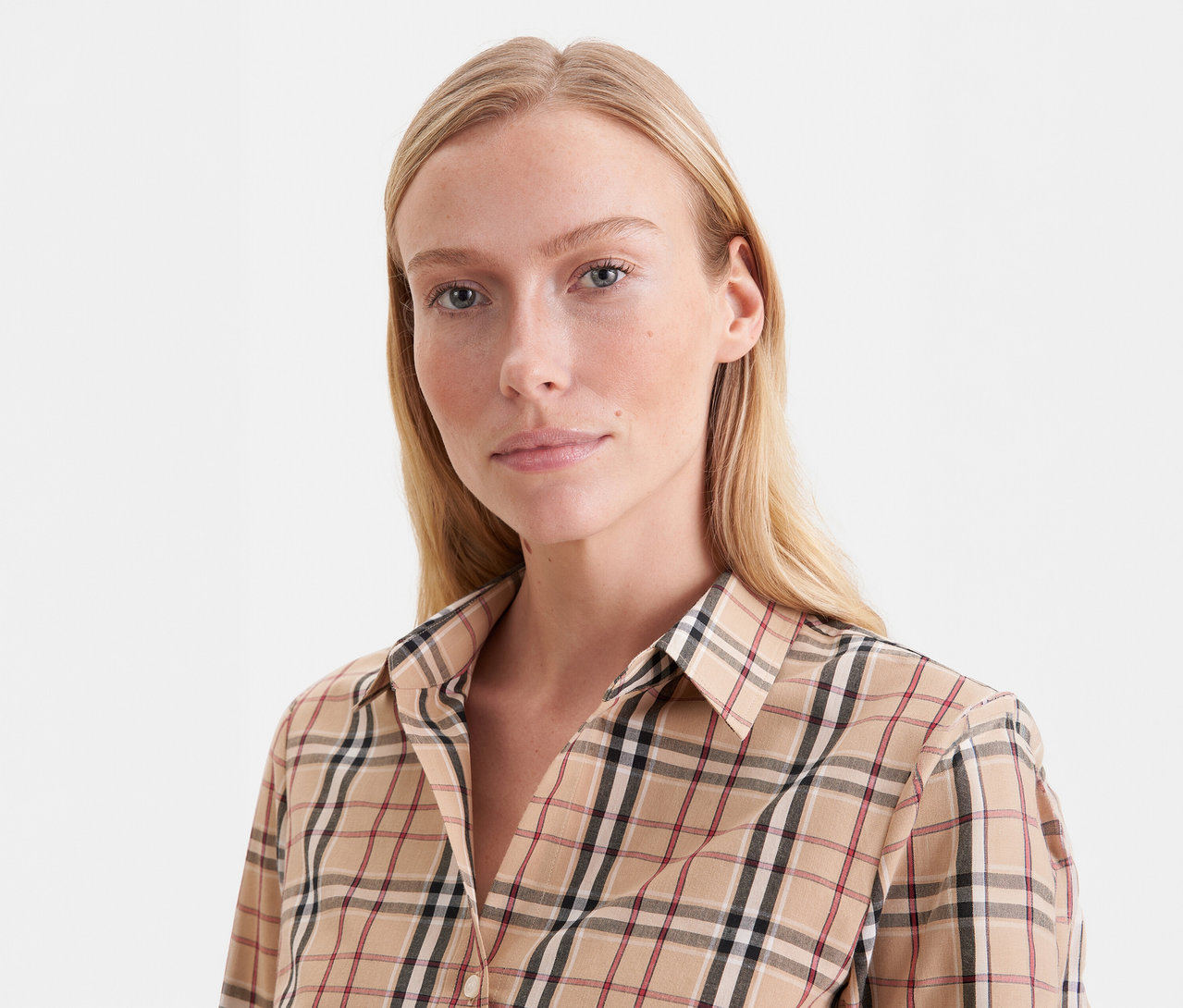 Gros plan d'une femme blonde portant une chemise à carreaux beige avec des lignes noires, blanches et rouges.
