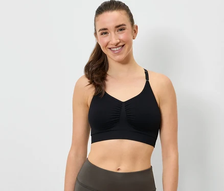Une femme souriante porte un soutien-gorge de sport noir et un legging gris.