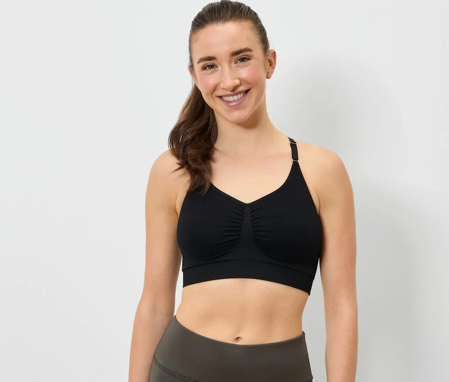 Une femme souriante porte un soutien-gorge de sport noir et un legging gris.